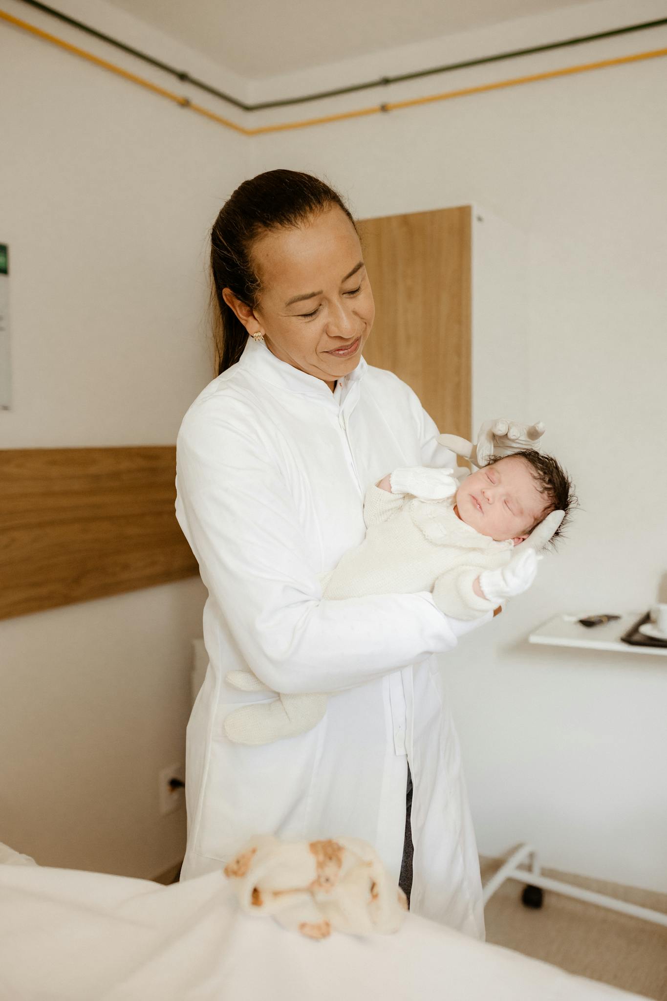 A caring healthcare professional holds a newborn baby in a hospital room with a warm smile.